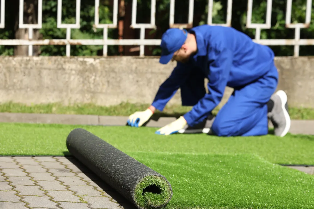 Artificial turf being rolled out across a prepared backyard base